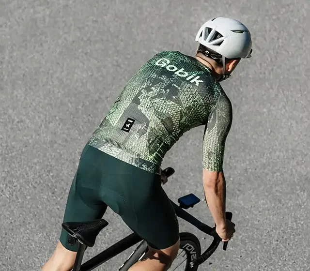 Kolesar od zadaj v zelenem kolesarskem dresu Gobik Glitch Mode na cestnem kolesu.